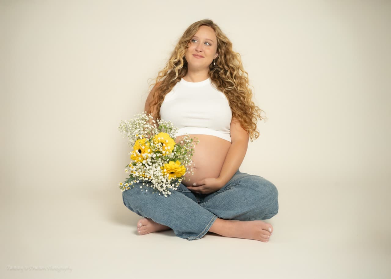 Bethany Youngdale seated during pregnancy and holding a bouquet of yellow flowers